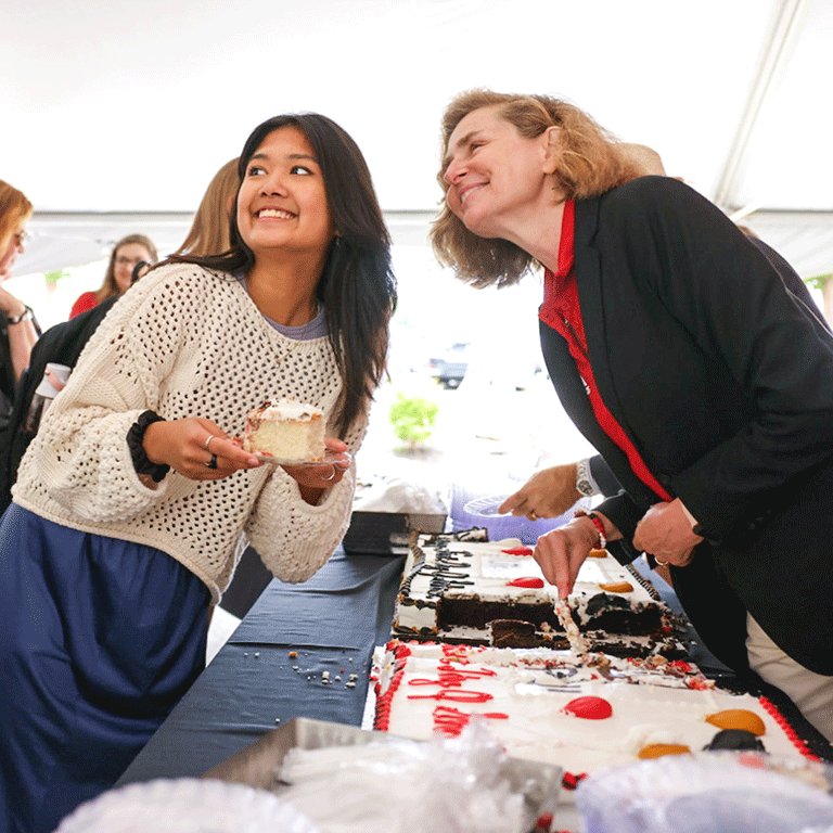 A girl poses with President Whitten while holding cake.