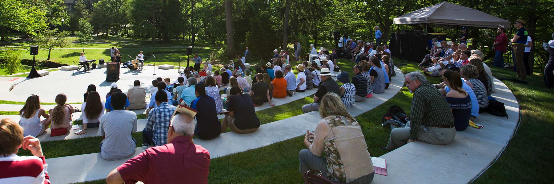 A crowd sits on the steps of the Prebys Amphitheater to watch an outdoor music concert on a summer day