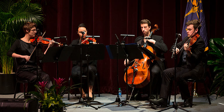 A string quartet plays in front of a red velvet curtain at an event.
