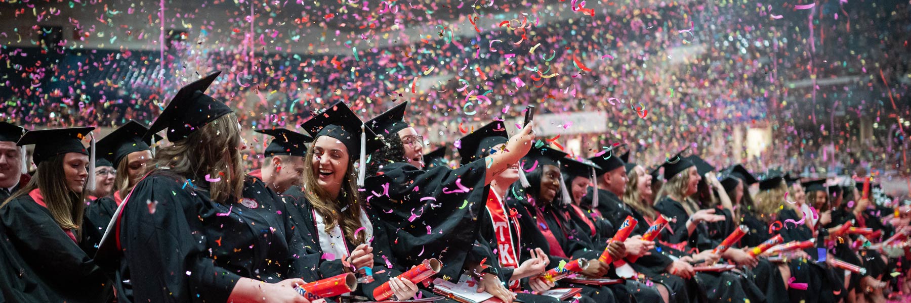 A crowd of university graduates laugh as confetti falls.