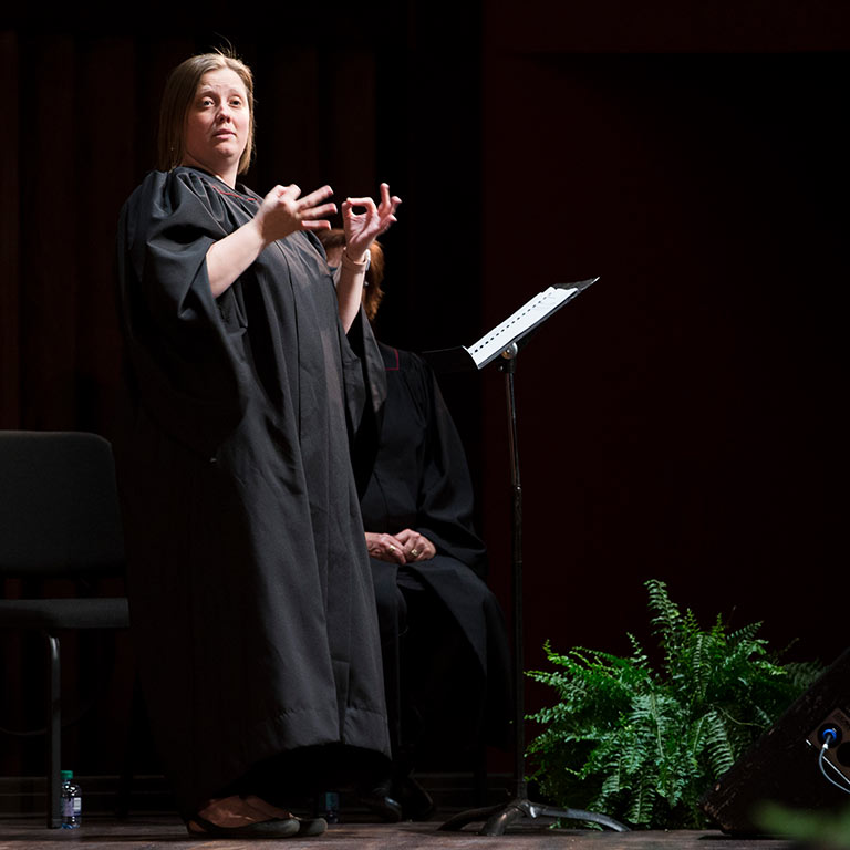 A sign language interpreter translates a formal academic event into ASL for the audience.