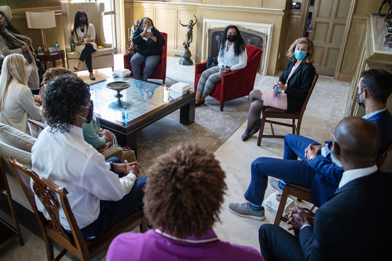 A visually diverse group of young people wearing business attire and COVID masks consult together in a formal drawing room. 